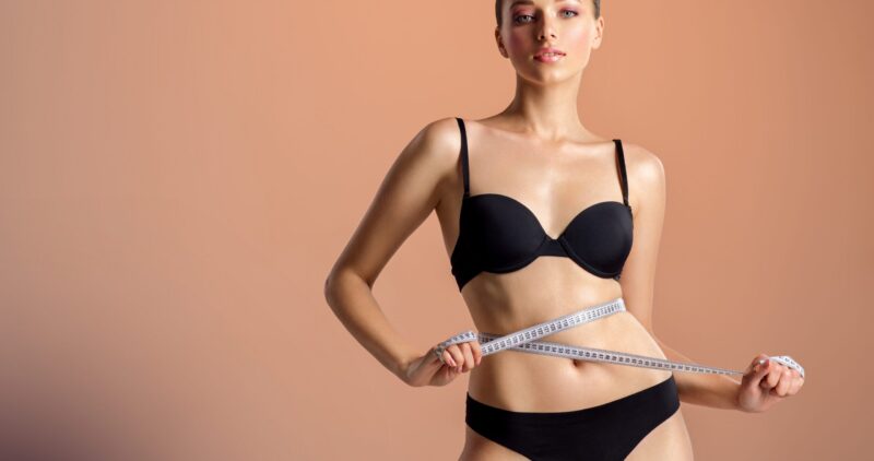 Young woman with tape and a beautiful, healthy body. Sexy woman measuring her perfect body. Young girl in black underwear with an ideal body, posing with a metre. Woman measuring her waist.